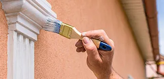 A person painting the exterior of a house with a brush, adding color and life to the building's facade.